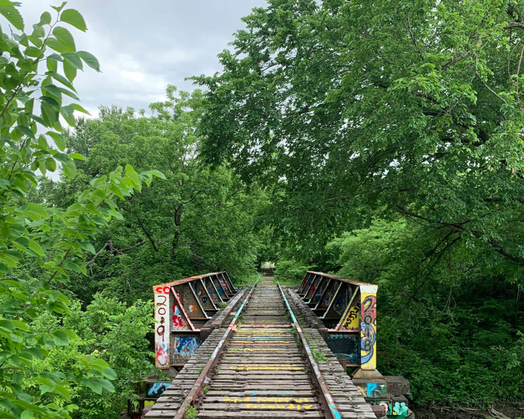 Graffiti-covered train tracks and bridge surrounded by lush green trees in Allen TX
