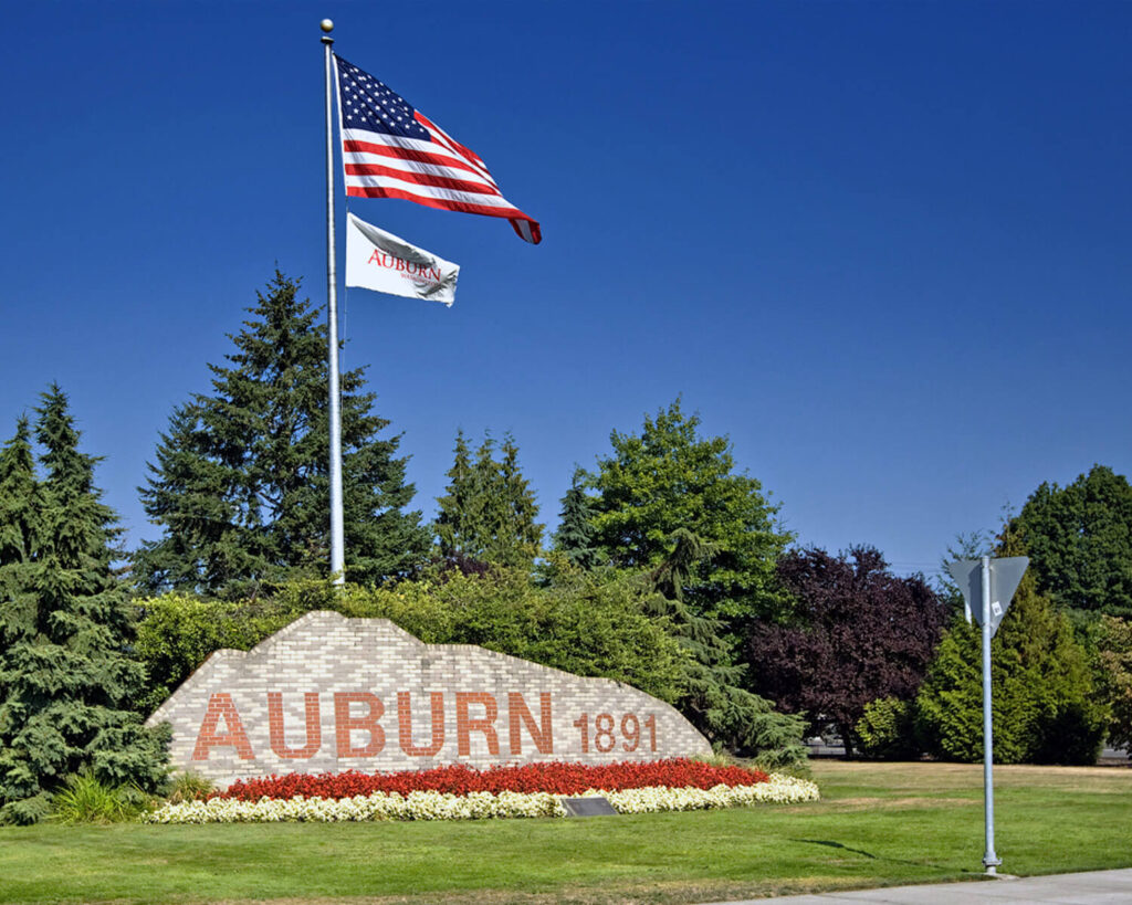 Welcome sign for Auburn, Washington with American flag and flowers under a clear blue sky