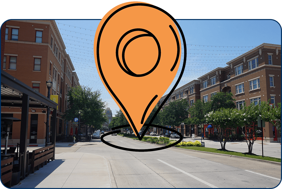 Large location pin icon on Coleman Boulevard in downtown Frisco TX lined with red brick buildings, trees, and shops under string lights