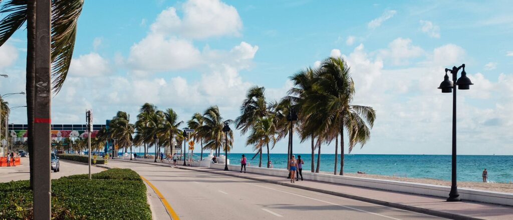 Fort Lauderdale Beach FL with palm-lined road, ocean views, and people walking along the beachfront