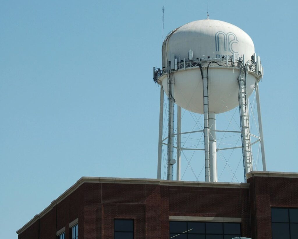 McKinney TX water tower rising above red brick building, a well-known city landmark against blue sky