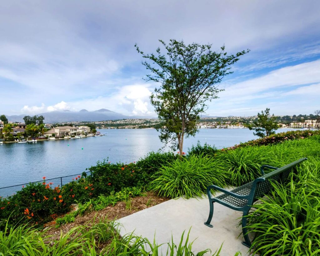 Scenic view of Lake Mission Viejo in California with a park bench, greenery, and waterfront homes