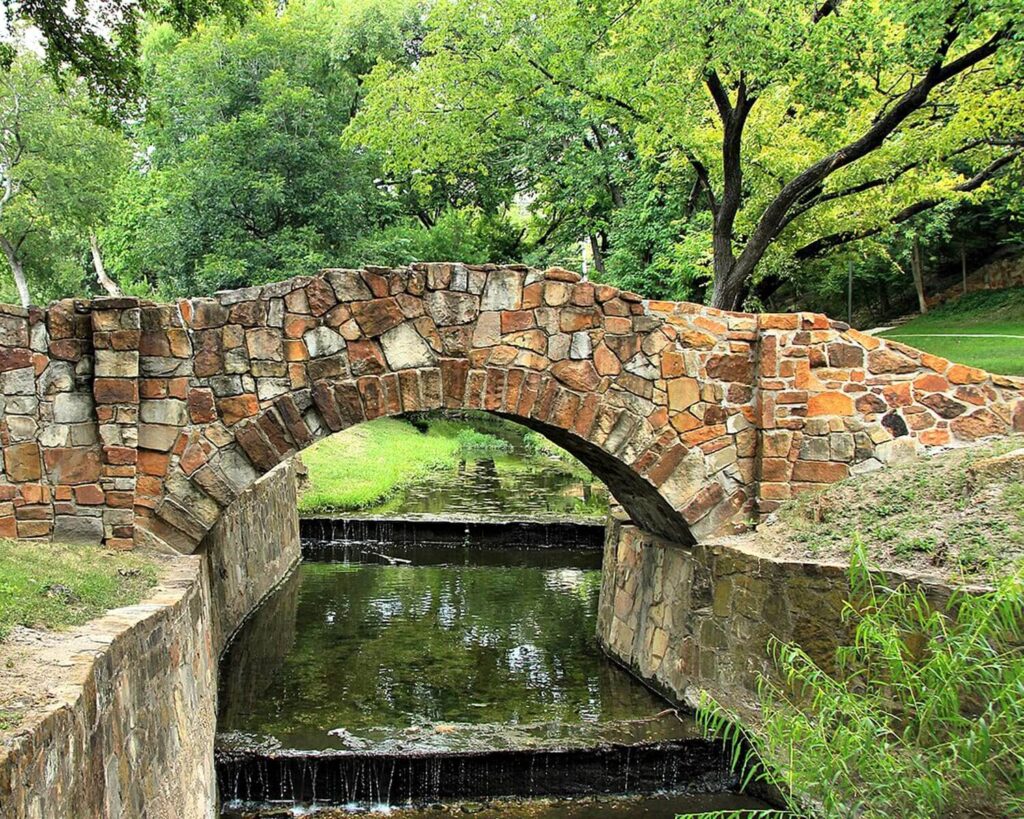 Stone bridge over Turtle Creek in Reverchon Park Oak Lawn surrounded by lush green trees
