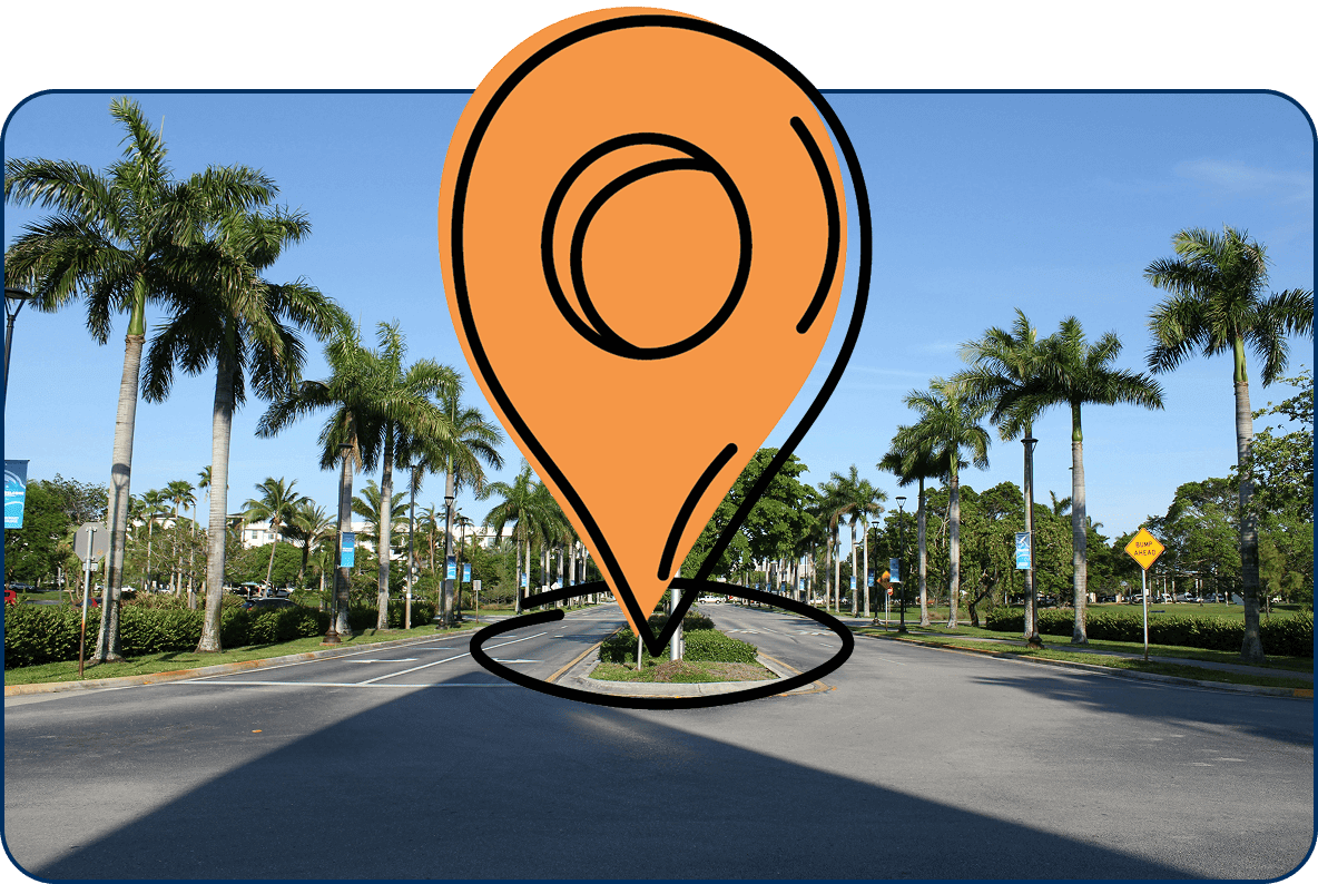 Large location pin icon on palm tree-lined street in Pinecrest, Florida under a clear blue sky with tropical greenery and signs