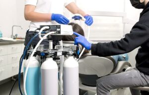 Dental team preparing patient for treatment using sedation equipment with gas tanks