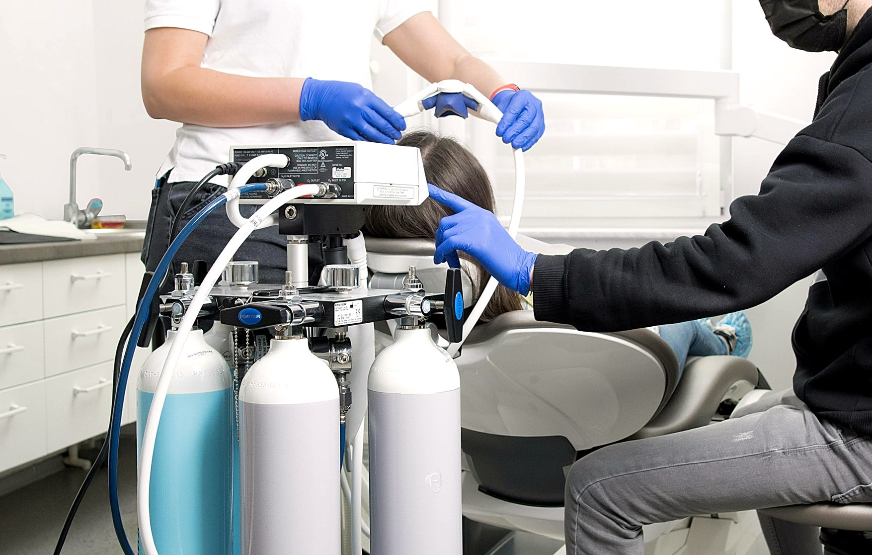 Dental team preparing patient for treatment using sedation equipment with gas tanks