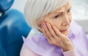 Woman experiencing toothache at dentist and holding jaw in pain