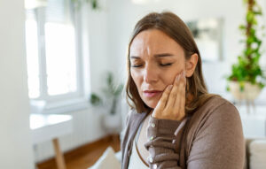 Woman holding her jaw in pain at home, experiencing severe tooth pain