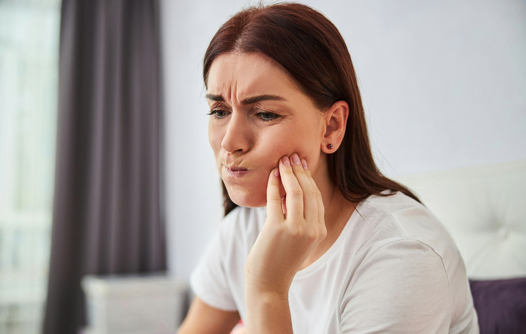 Woman holding her jaw in pain, experiencing a severe toothache at home