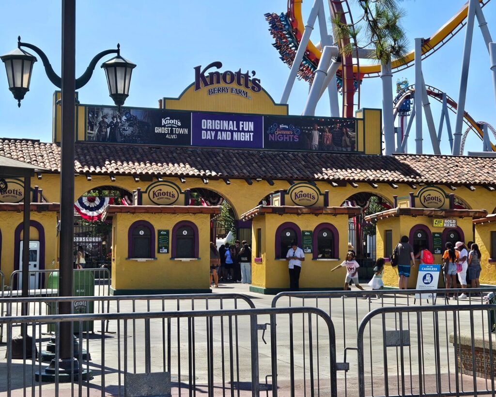 Knott’s Berry Farm entrance with ticket booths, visitors, and roller coasters in background in California theme park