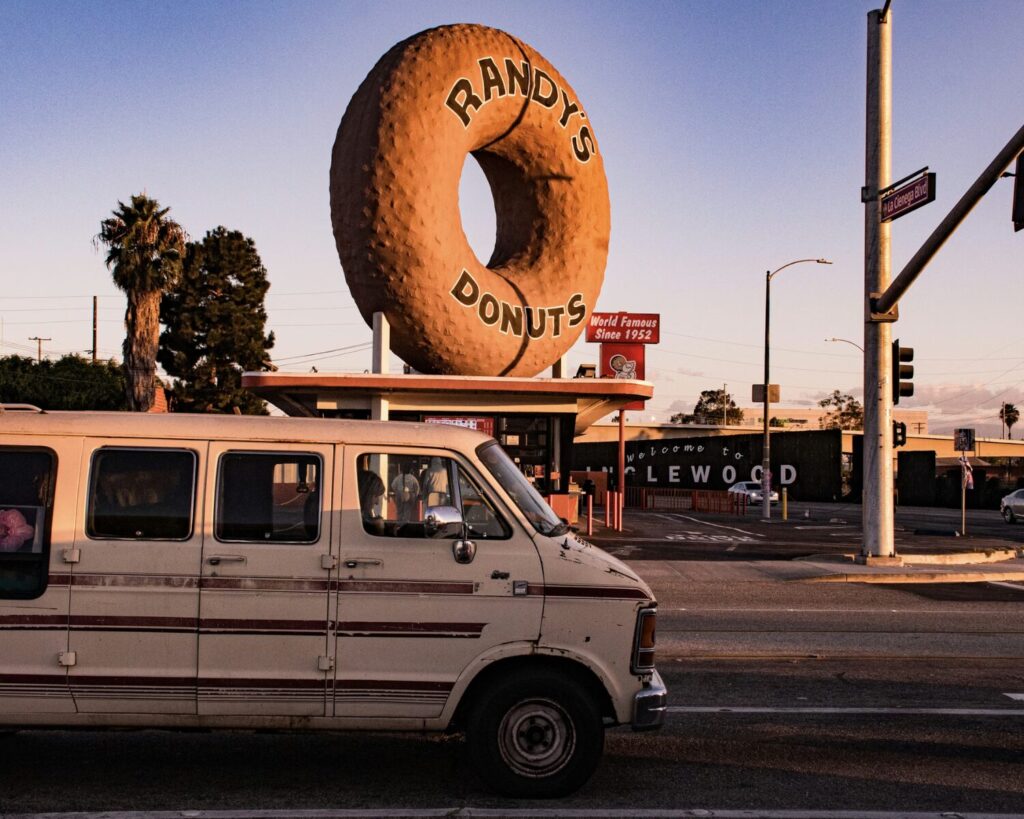 Van passing Randy’s Donuts landmark in Inglewood Los Angeles with giant donut sign at street intersection