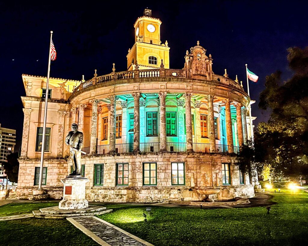 Coral Gables City Hall in Miami Florida USA illuminated at night with historic architecture columns clock tower and statue in front lawn
