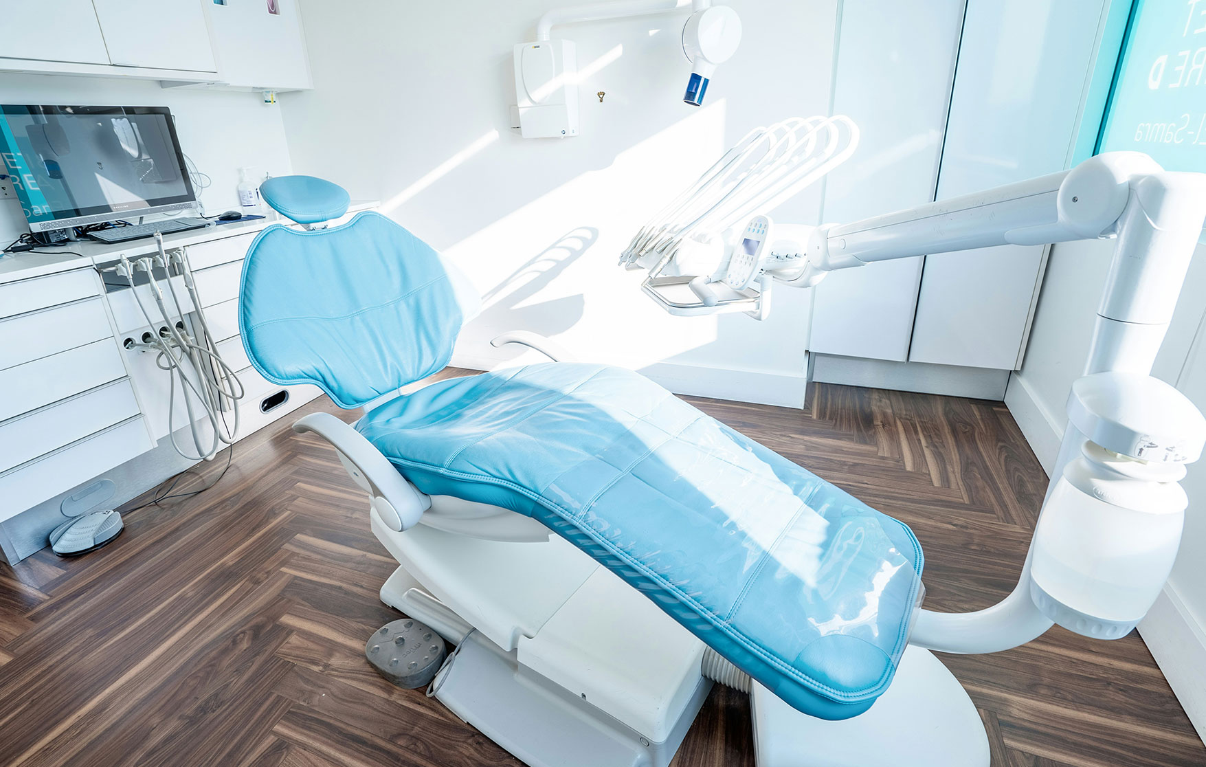 Modern dental exam room with blue reclining dentist chair and overhead equipment