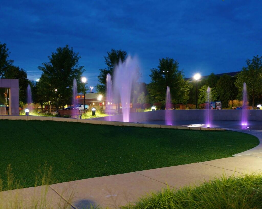 Elk Grove Village Illinois park fountain at night with colorful lights water features and landscaped public space