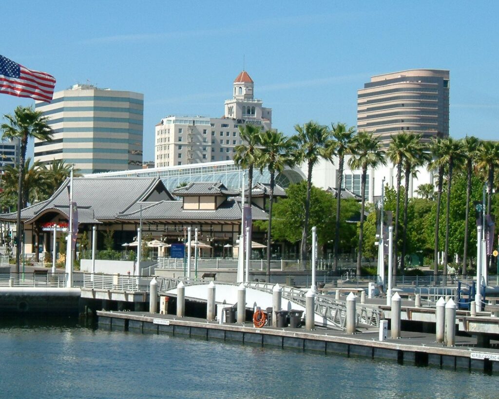 Long Beach California waterfront with marina docks palm trees American flag and city skyline buildings on a sunny day