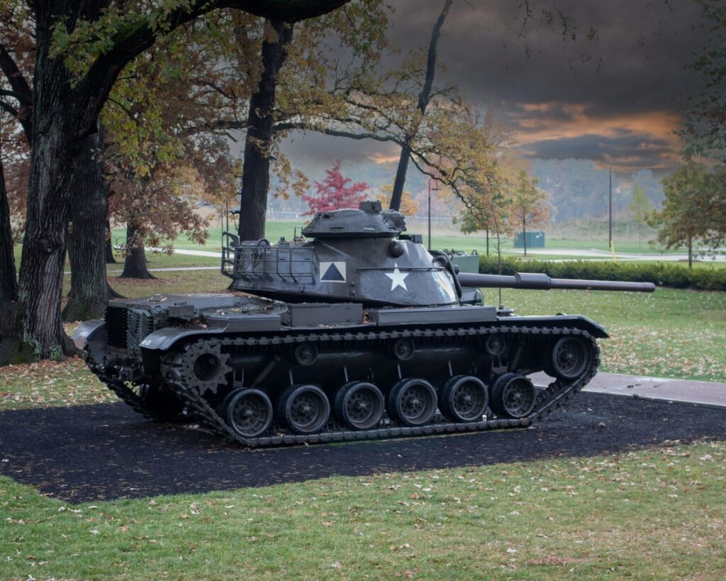 Military tank displayed in park surrounded by trees autumn landscape outdoor museum setting cloudy sky background