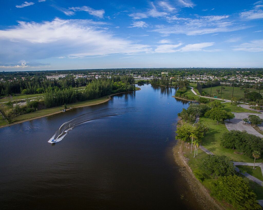 Lake in Pembroke Pines Florida with boat on water scenic aerial view green landscape and residential surroundings under blue sky