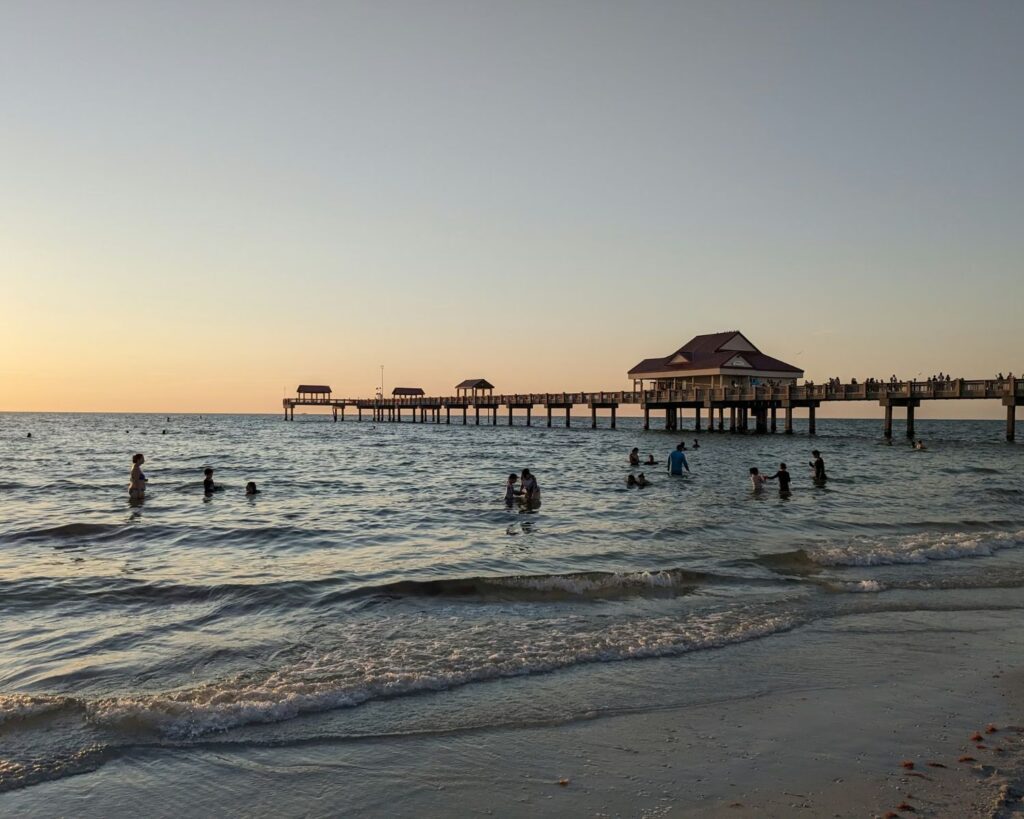 People swimming in ocean near pier during sunset beach waves coastal scene relaxing vacation lifestyle seaside evening