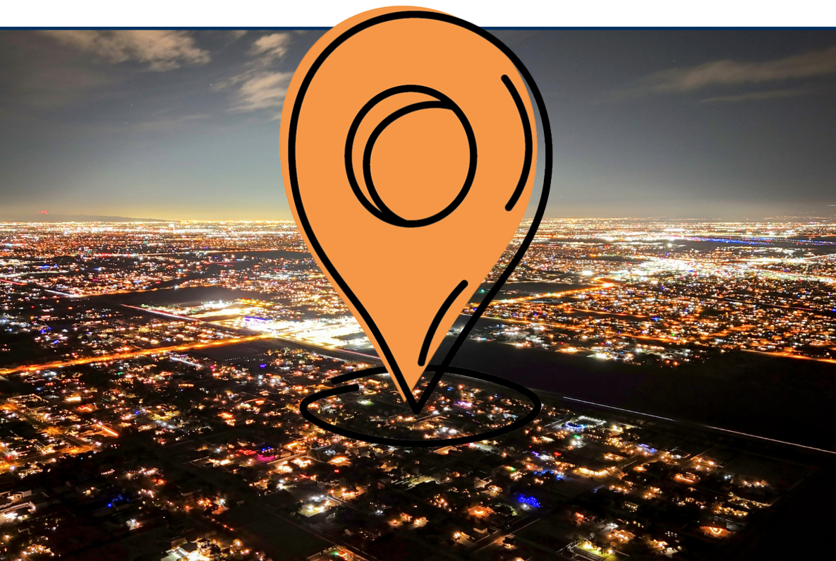 Aerial nighttime view of Queen Creek, Arizona, showing a wide cityscape filled with glowing streetlights, illuminated roads, and clusters of residential buildings stretching toward the horizon under a dark sky.