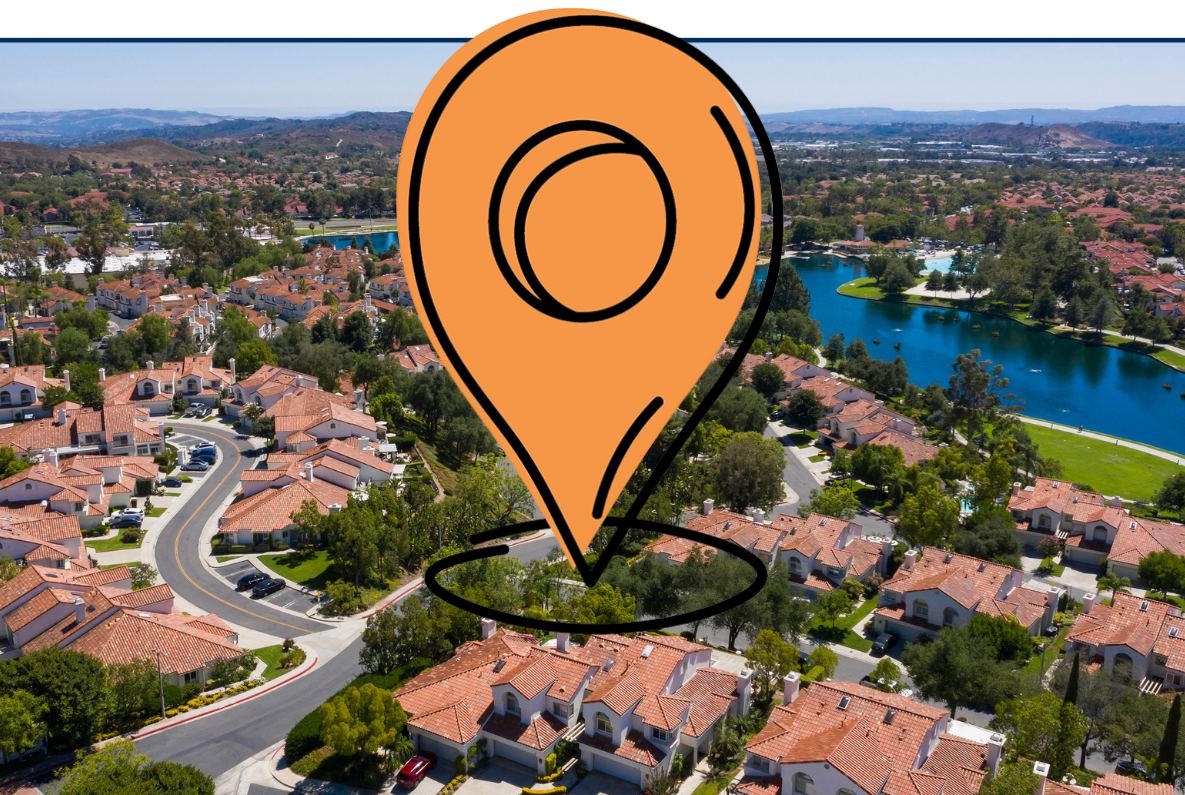 Aerial view of Rancho Santa Margarita, California, showing a suburban neighborhood with rows of houses, curved streets, green trees, and a bright blue lake surrounded by residential areas and rolling hills in the distance.