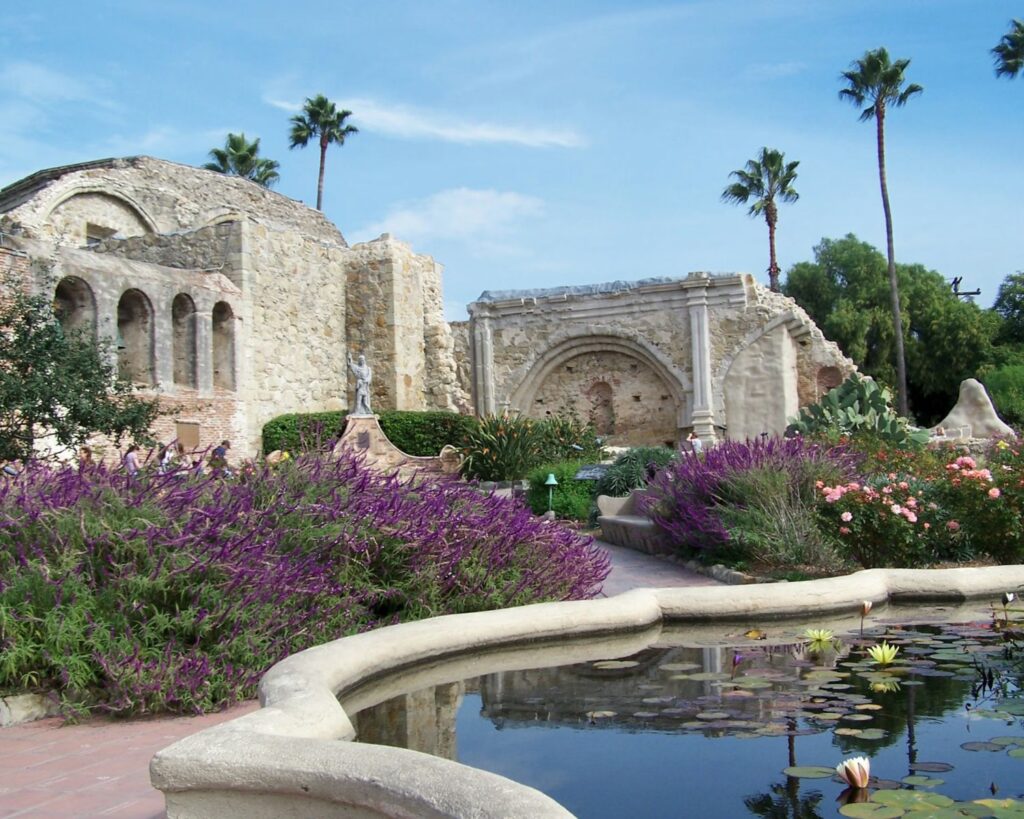 Historic Mission San Juan Capistrano garden with stone arches pond flowers and palm trees in California daytime