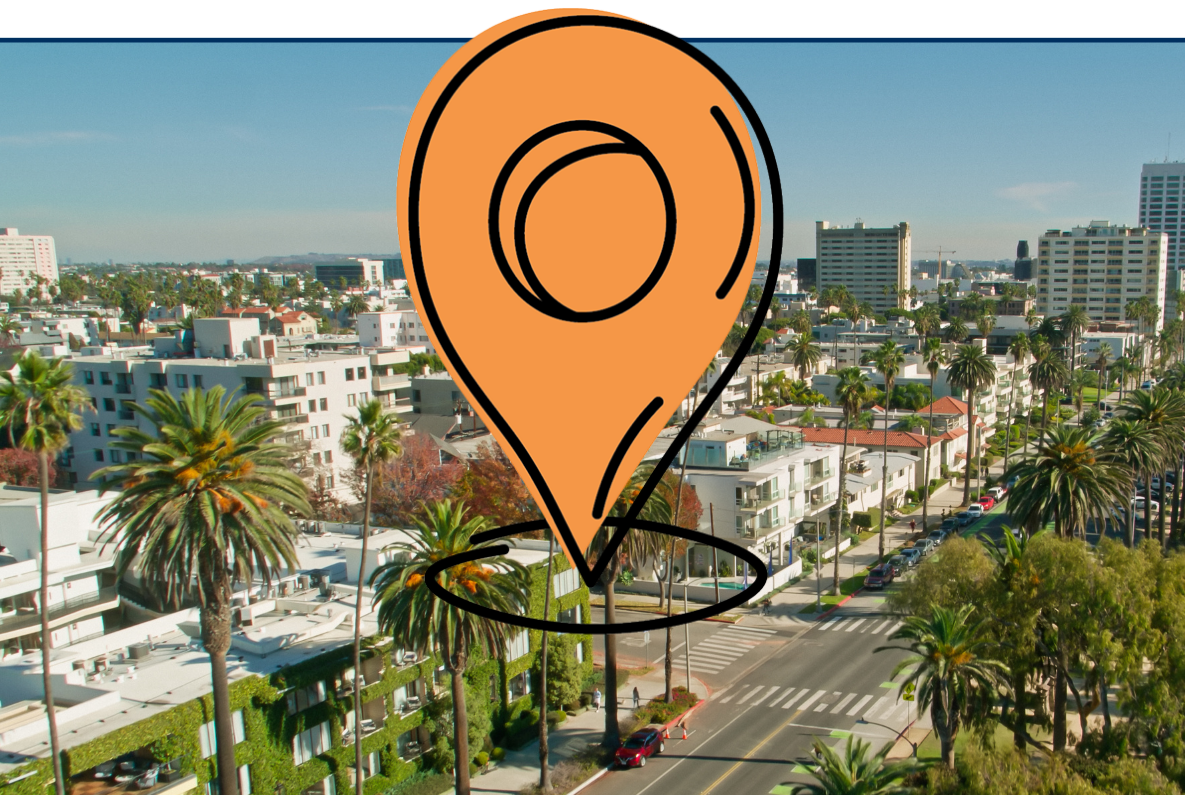 Aerial view of Santa Monica, California, showing palm-lined streets, residential buildings, and a coastal road running alongside a sandy beach and the ocean on a clear sunny day.