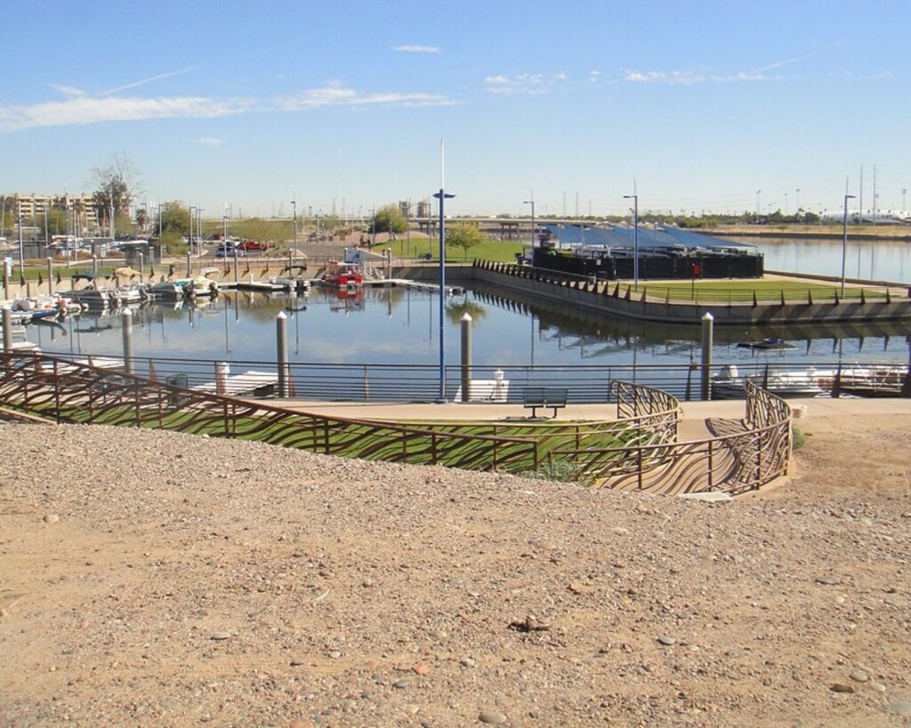 Tempe Town Lake marina with small boats docked along calm water, walking paths with railings, and open landscape under a clear blue sky