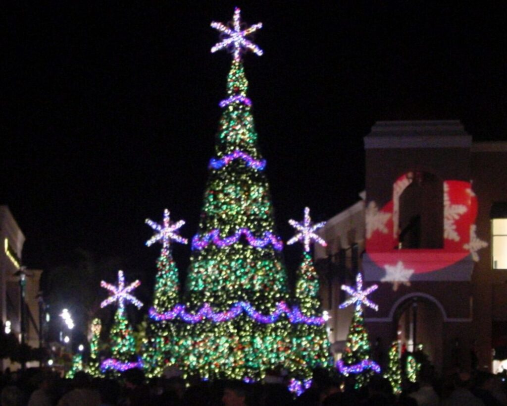 Night view of The Shops at Wiregrass in Wesley Chapel Florida decorated with Christmas lights, illuminated storefronts and a large holiday tree