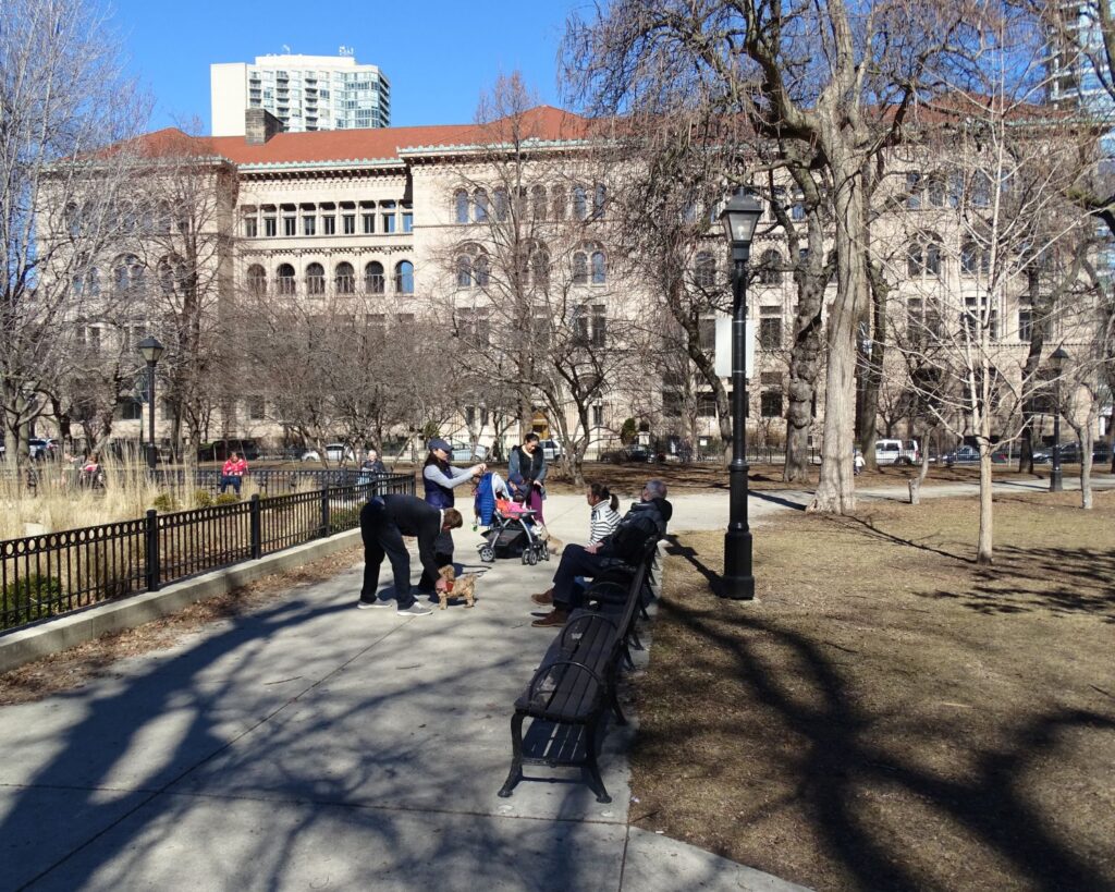Washington Square Park Chicago Gold Coast with people walking sitting on benches trees pathway and historic buildings in background