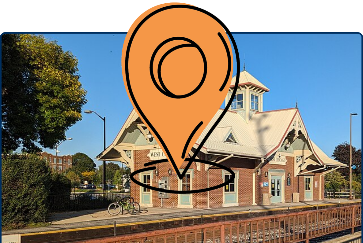 West Chicago Metra station building beside train tracks with platform railings and a clear blue sky