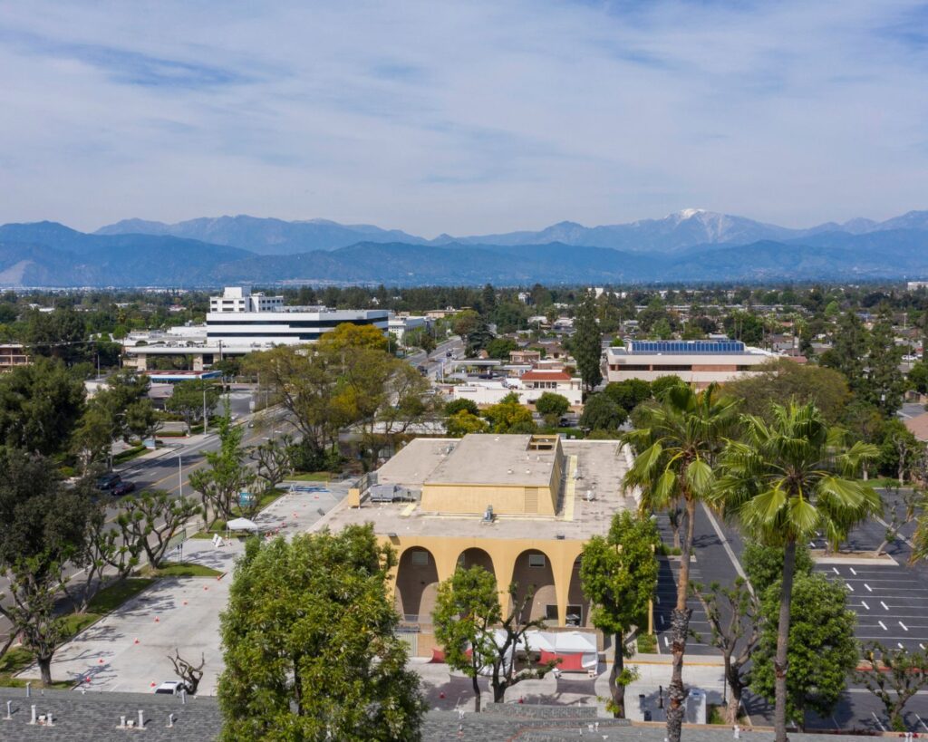 West Covina California aerial view with residential buildings palm trees streets and mountains in background under clear sky