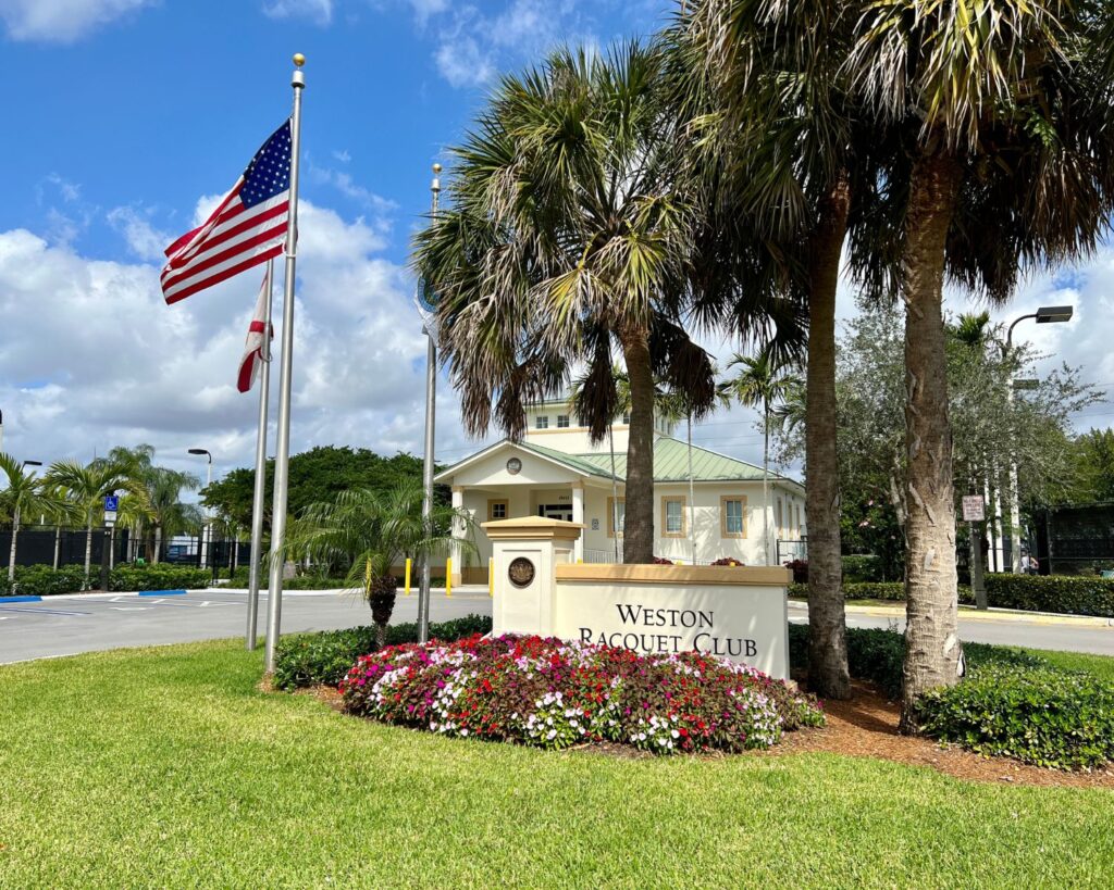 Entrance of Weston Racquet Club Weston Florida with palm trees American flag and landscaped garden area