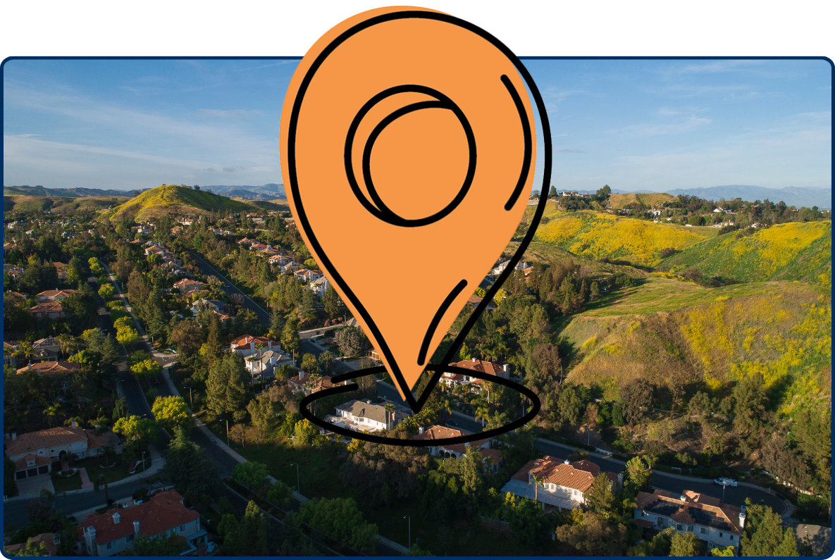 Aerial view of Calabasas, California, showing hillside residential neighborhoods surrounded by rolling green mountains covered in yellow wildflowers under a blue sky