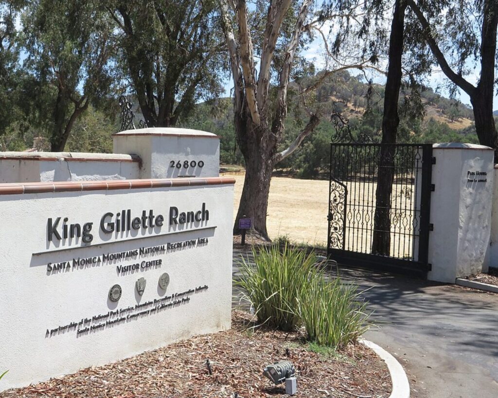 Entrance sign and gated driveway for King Gillette Ranch Visitor Center in the Santa Monica Mountains National Recreation Area, surrounded by trees and dry hillsides in California.