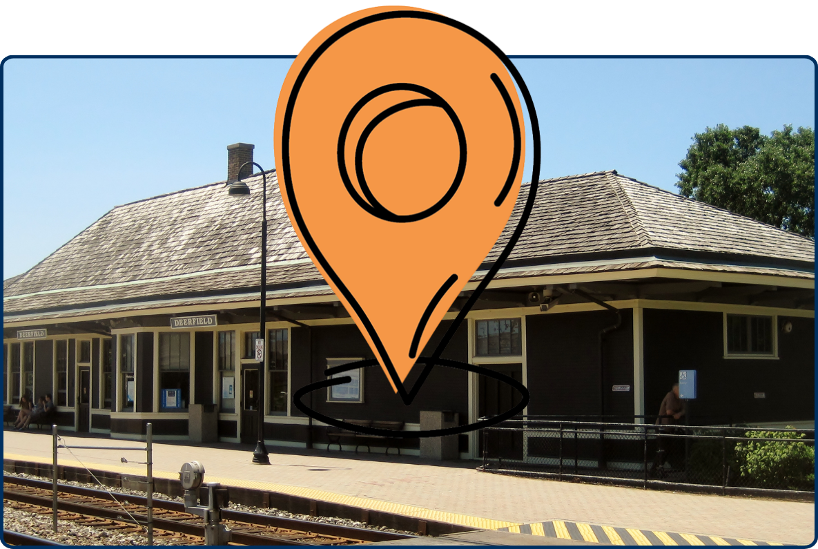 Historic Chicago, Milwaukee and St. Paul Railway passenger depot building beside railroad tracks, featuring a long covered platform and dark wood exterior under a clear blue sky.
