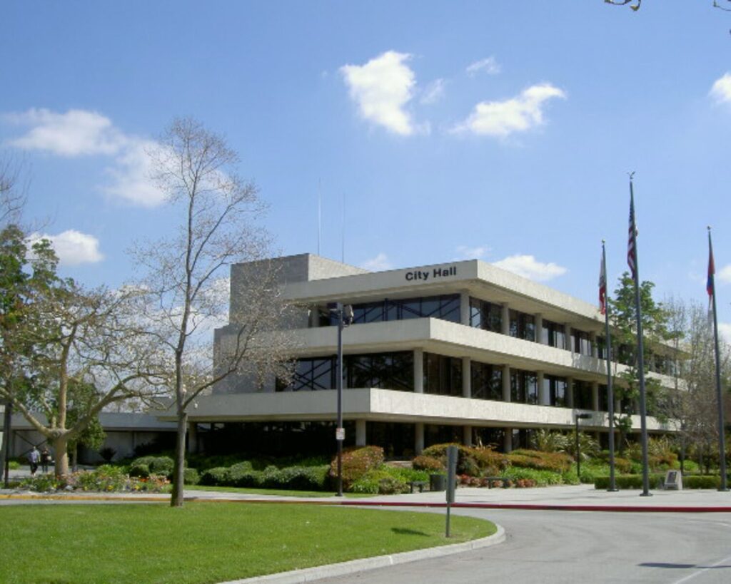 Downey City Hall building with landscaped lawn, trees, and flags under a clear blue sky.