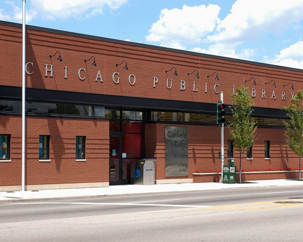 Exterior view of Chicago Public Library Garfield Ridge Branch, a red brick library with a glass entrance and street elements in front.