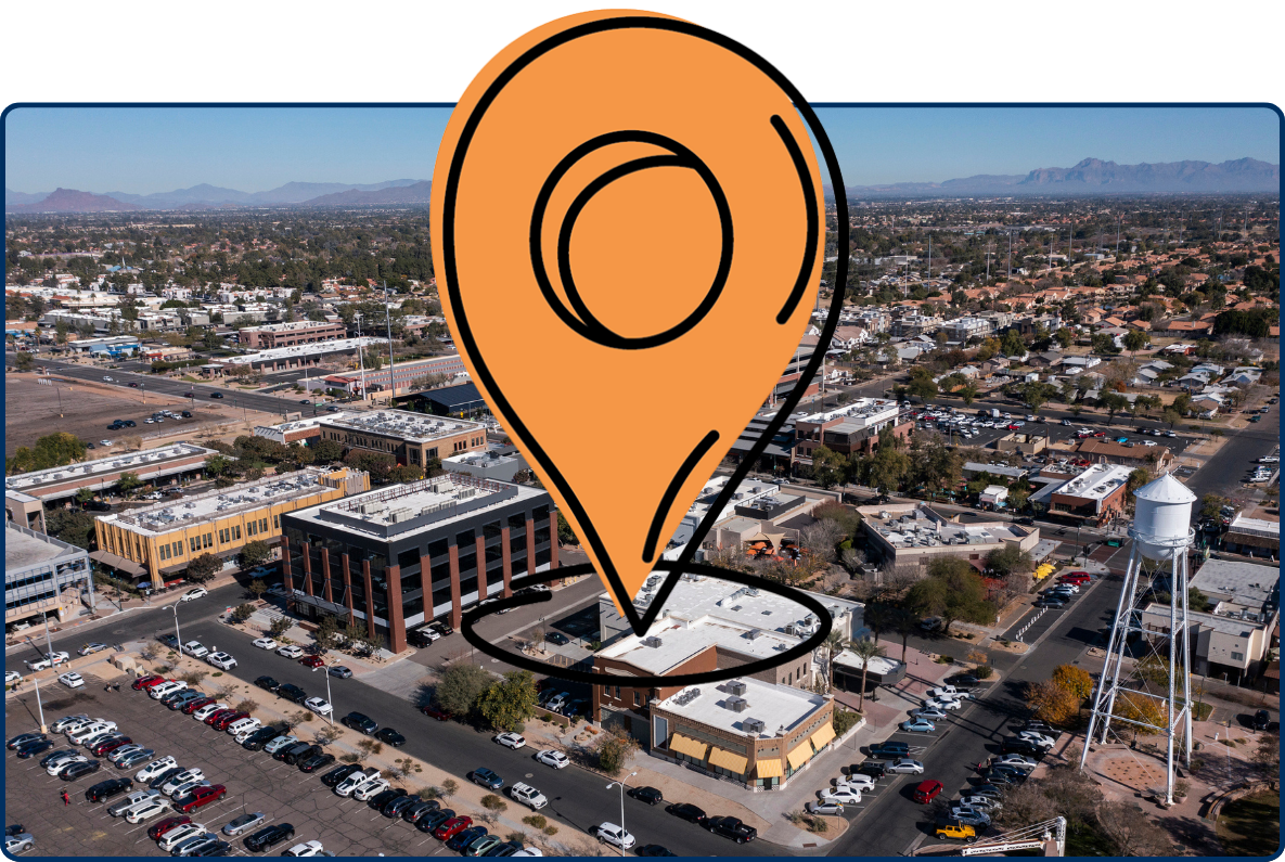 Aerial view of Gilbert, Arizona with suburban neighborhoods, commercial buildings, and distant mountains under a clear sky.