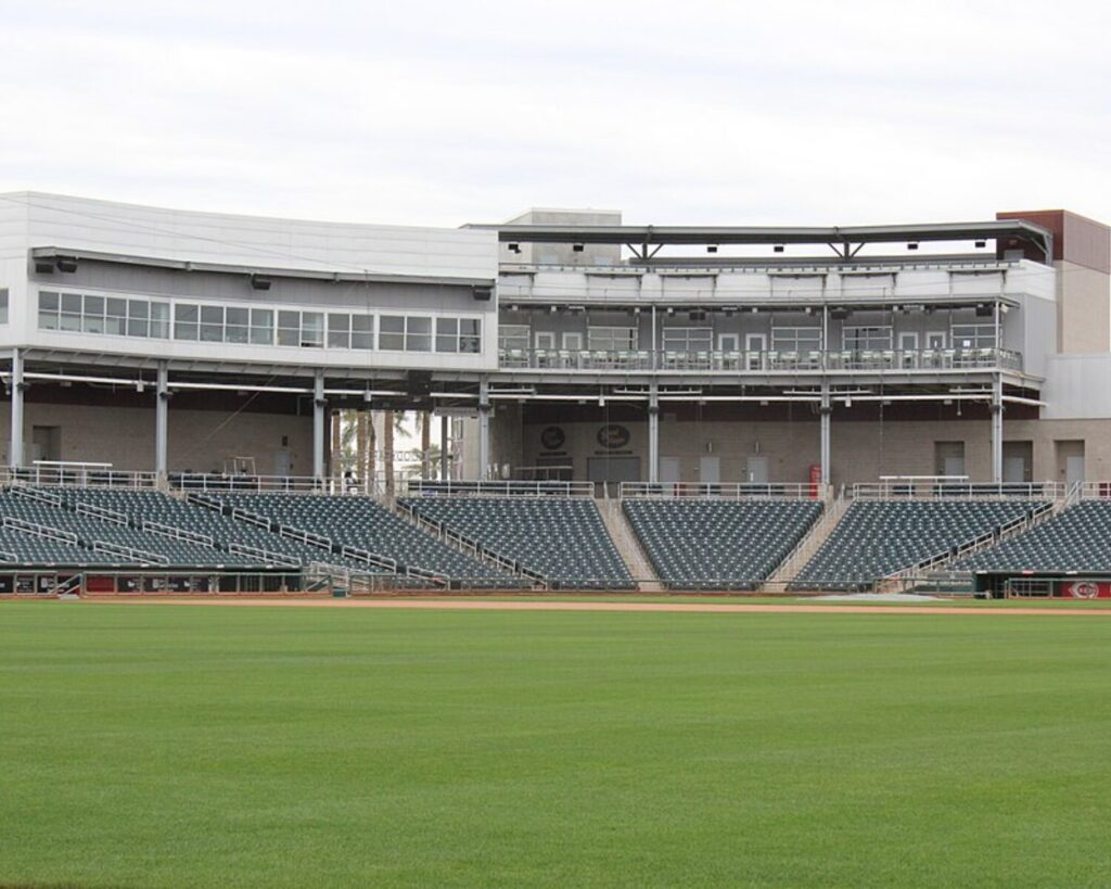 Empty baseball stadium at Goodyear Ballpark in Arizona, featuring green grass field, rows of gray seats, and a modern grandstand structure under an overcast sky.