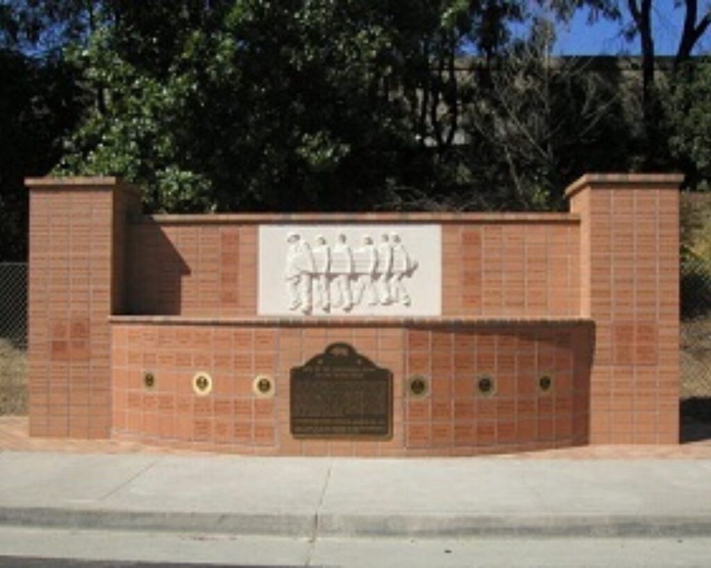 Brick memorial wall with a white relief panel showing a line of marching soldiers, flanked by brick pillars and plaques