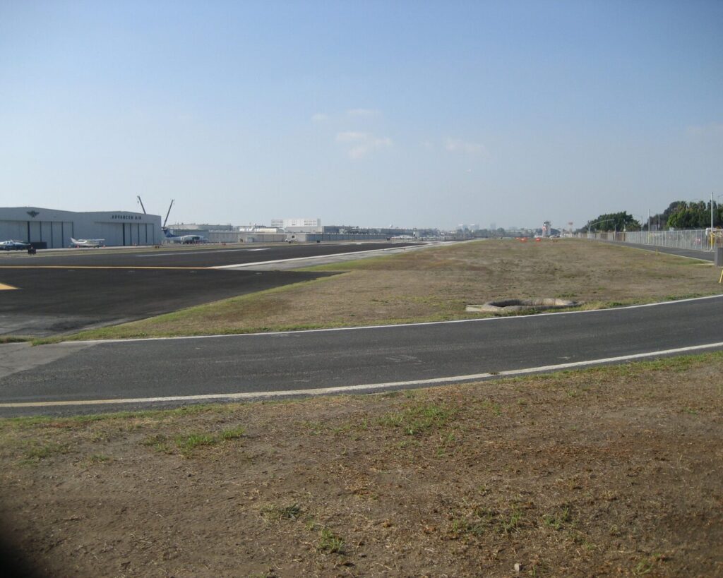 Hawthorne Municipal Airport runway with hangars and small aircraft in the distance under a clear sky.