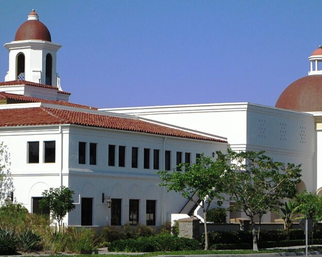 Laguna Hills Civic Center building with white walls, red-tiled domes, and landscaped greenery under a clear blue sky.