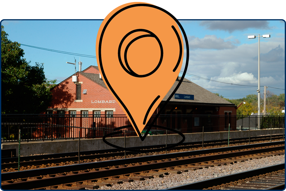 Lombard train station building beside railroad tracks, featuring a brick exterior, clock tower, and commuter rail platform under a partly cloudy sky.
