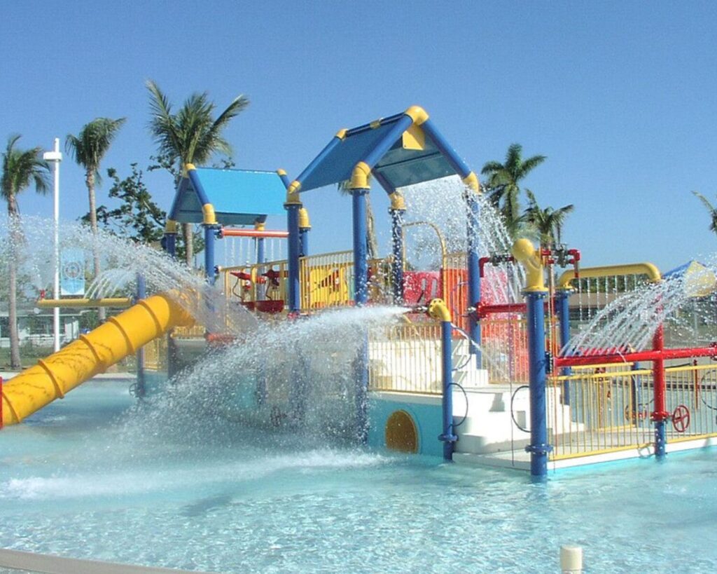 Colorful water playground at Calypso Cove Aquatic Facility with slides, fountains, and splashing water under clear sky.