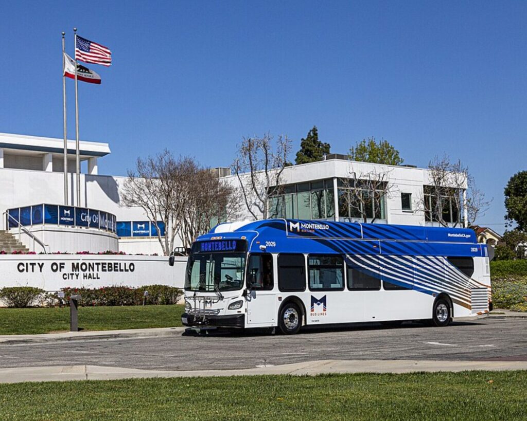 Montebello Bus Lines bus parked outside City of Montebello City Hall under a clear blue sky.