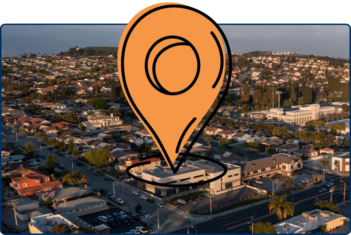 Aerial view of Montebello, California, showing residential neighborhoods, commercial buildings, and wide streets stretching across rolling hills at sunset.