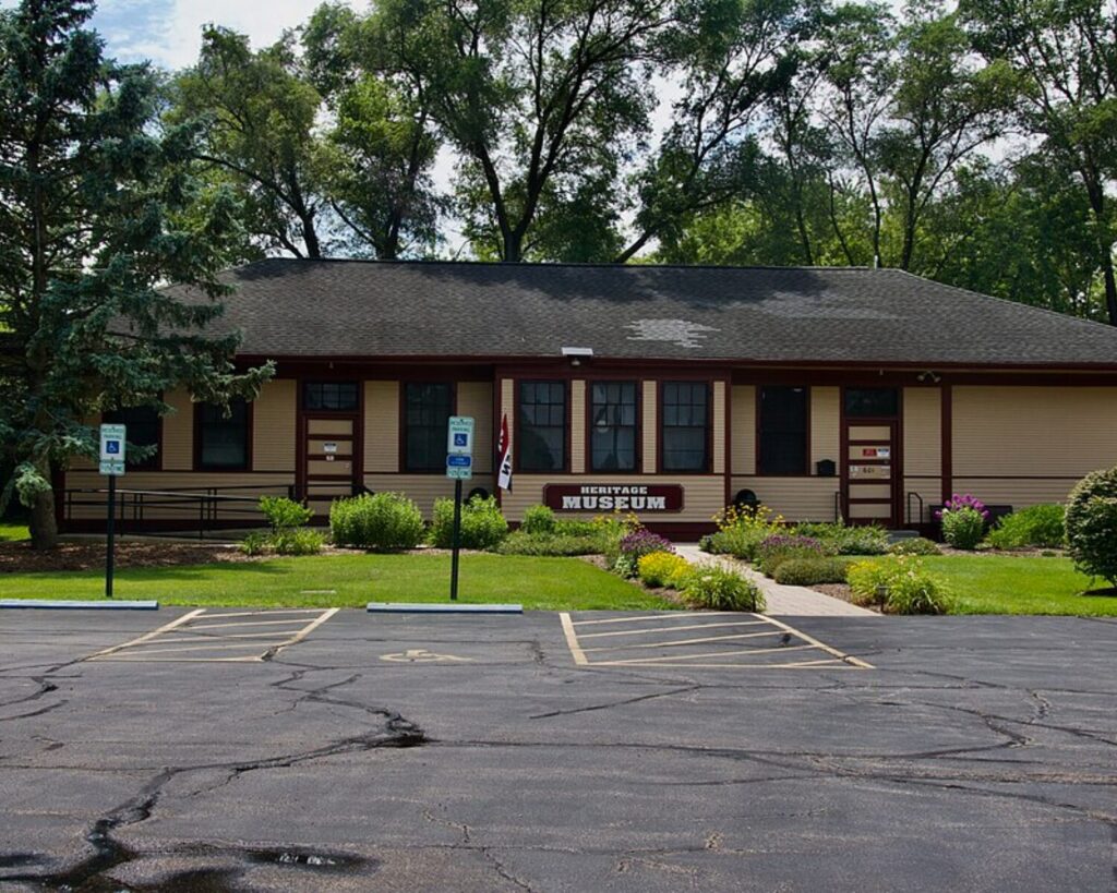 Front view of a single-story Heritage Museum building with beige siding, brown trim, and a manicured garden.