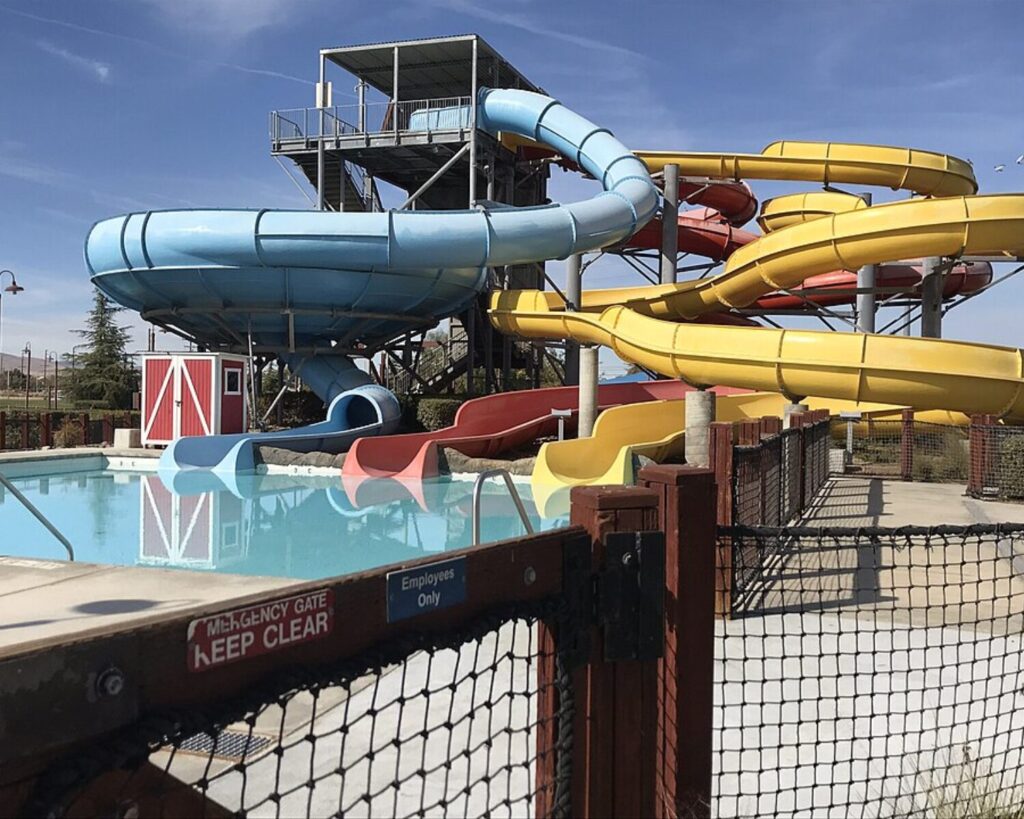 Water park slide tower with twisting blue, yellow, and red slides next to a swimming pool under a clear sky.