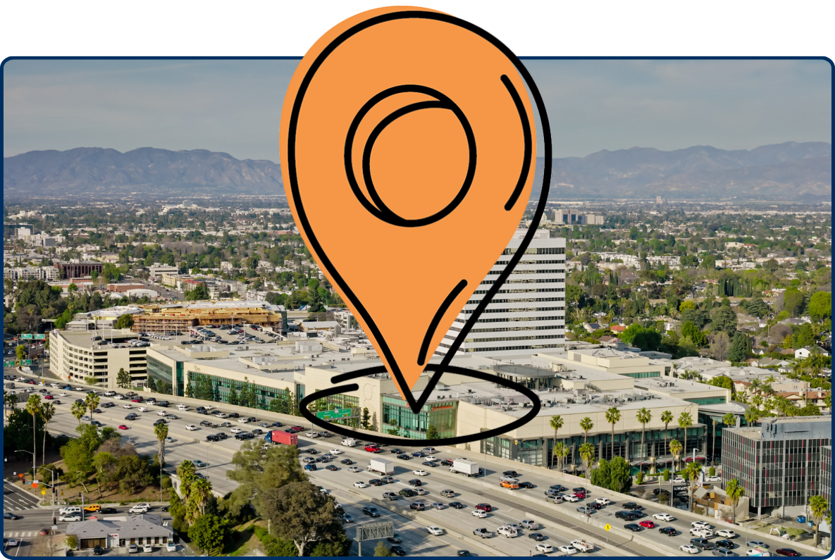 Aerial view of the San Diego Freeway in Sherman Oaks, California, with office buildings, traffic, residential areas, and mountains in the background.