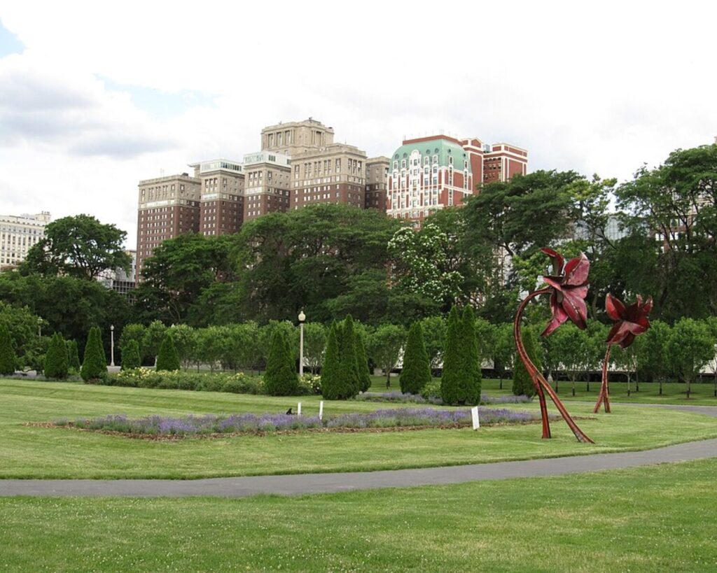 Scenic view of Grant Park near Congress Plaza, featuring open green lawns, landscaped gardens, and tree-lined paths with surrounding historic buildings and city skyline under a bright sky.